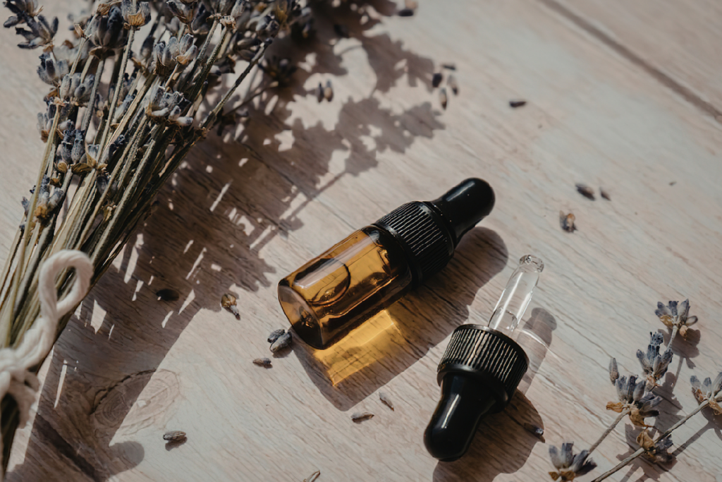 Dried lavender beside an amber oil bottle and glass dropper on a wooden surface