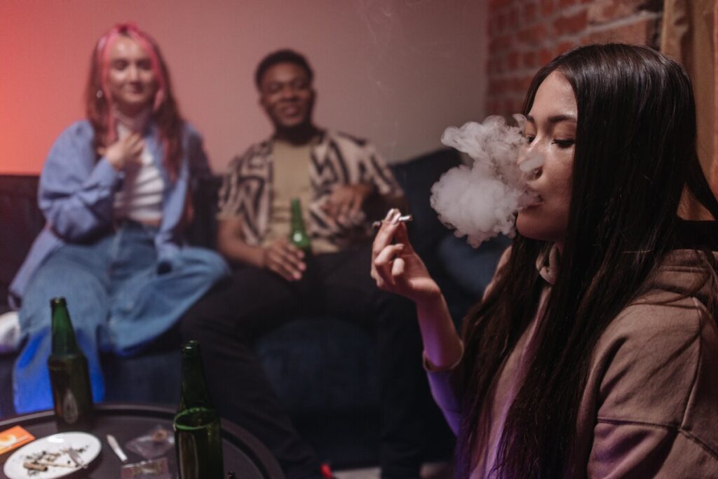 Young adults gathered indoors while one woman smokes a joint