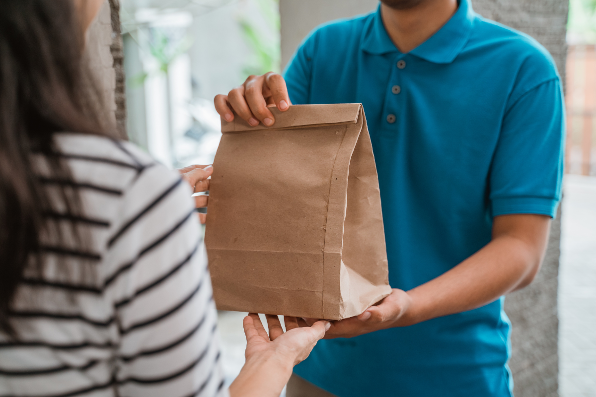 Delivery driver hands a brown paper bag to a customer at the door