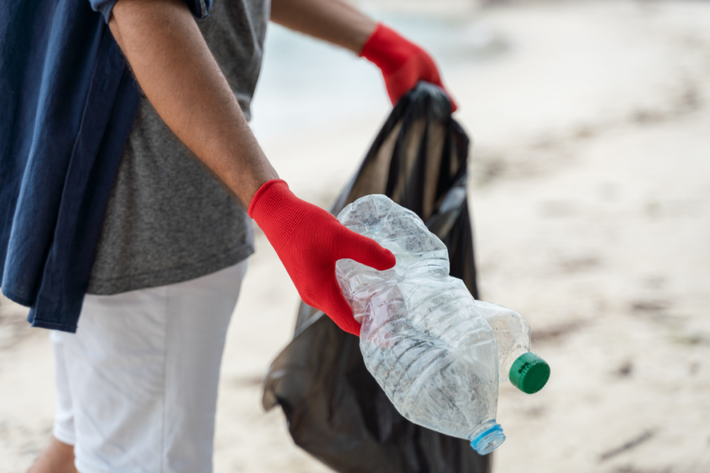 Volunteer wearing red gloves picks up plastic bottles during a beach cleanup