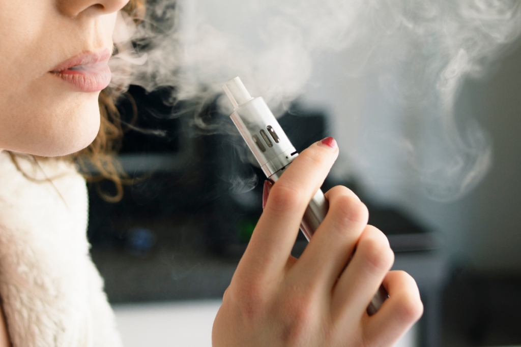 Close-up of a woman using a vape indoors with visible vapor