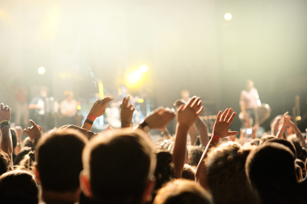 Concert audience raising their hands toward a brightly lit stage