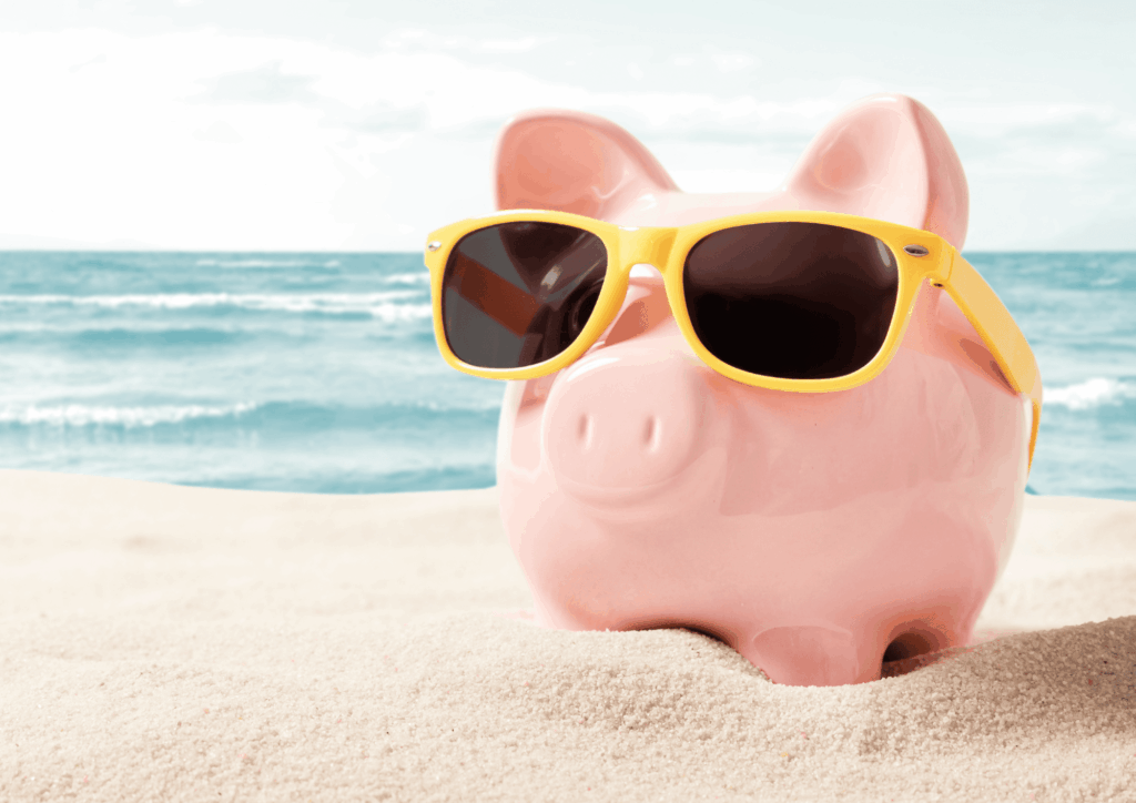 Pink piggy bank wearing yellow sunglasses on a sandy beach