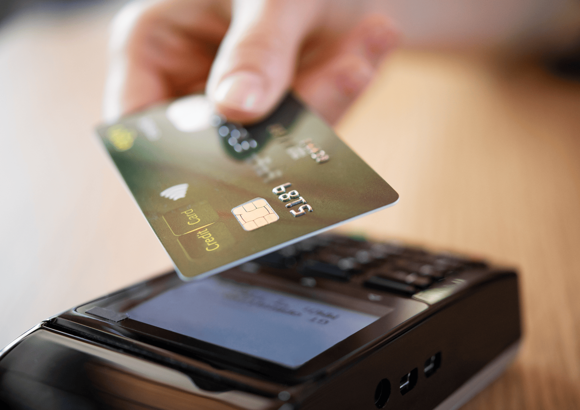Hand holding a credit card above an electronic payment terminal