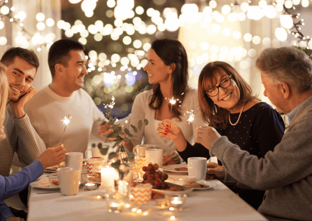 Family and friends gathered around a holiday dinner table holding sparklers